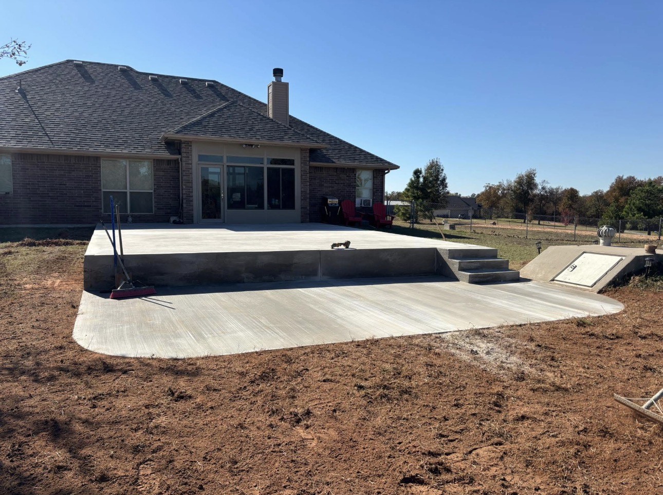 Large poured concrete patio with steps behind a brick house